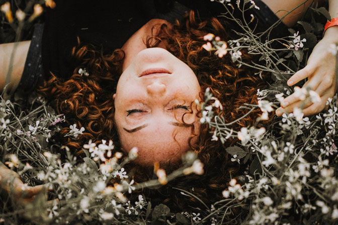 Zu sehen ist eine Frau, die in einer Blumenwiese liegt.