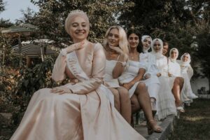 A group of guests lined up behind the bride sitting down in beautiful dresses