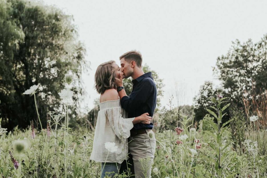 A couple kissing in the middle of a wild flowering field