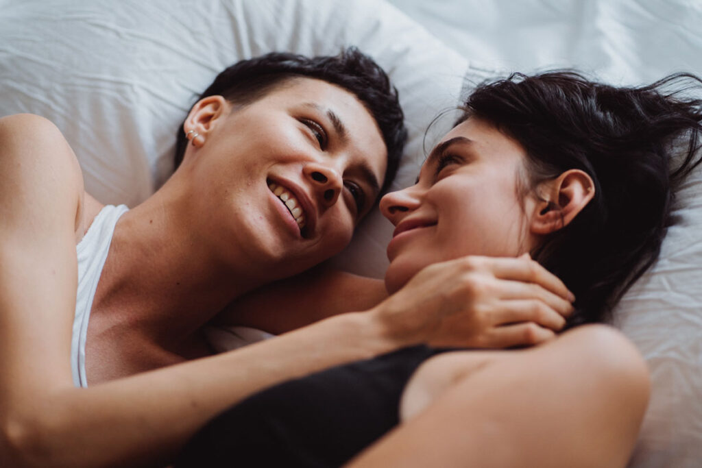 A couple lie in bed and smile at eachother