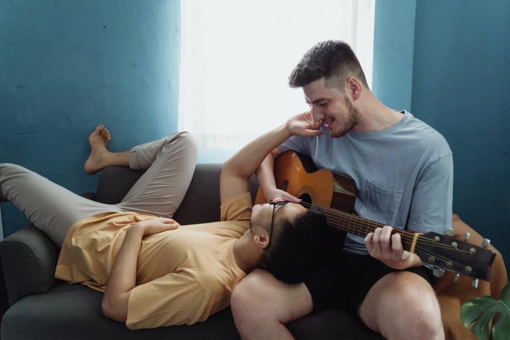 A plays guitar to his partner whose head is on his lap as a romantic gesture.