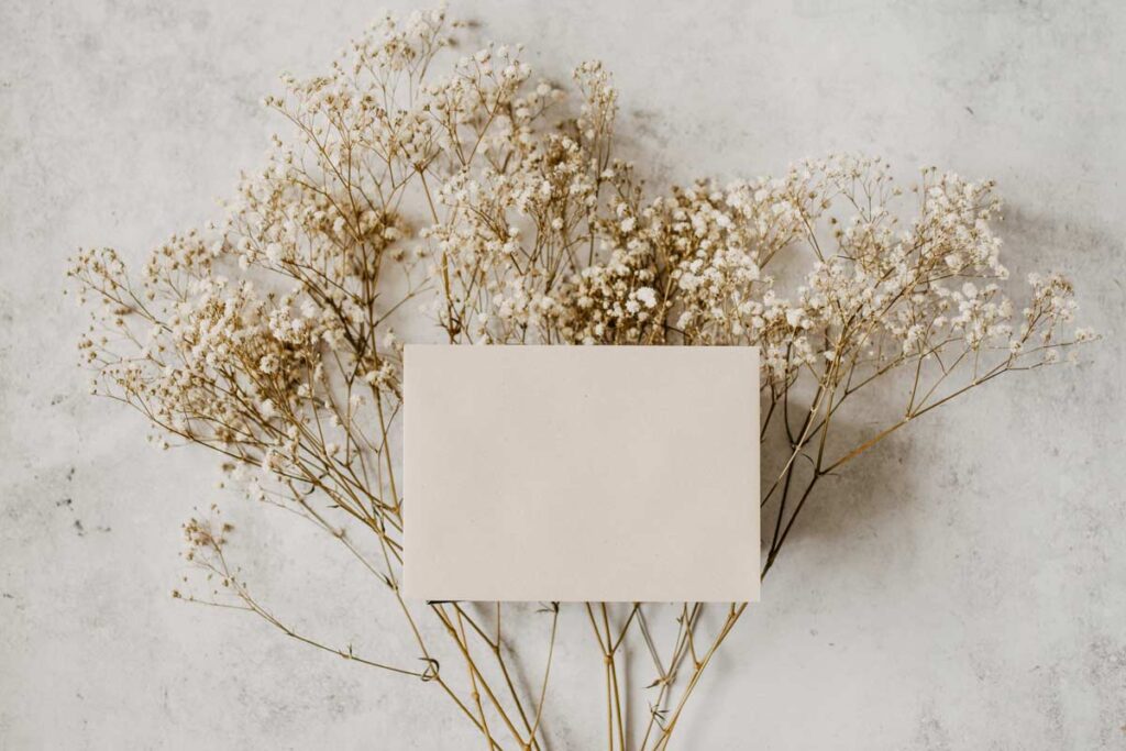 A blank card lies on top of a spray of white flowers