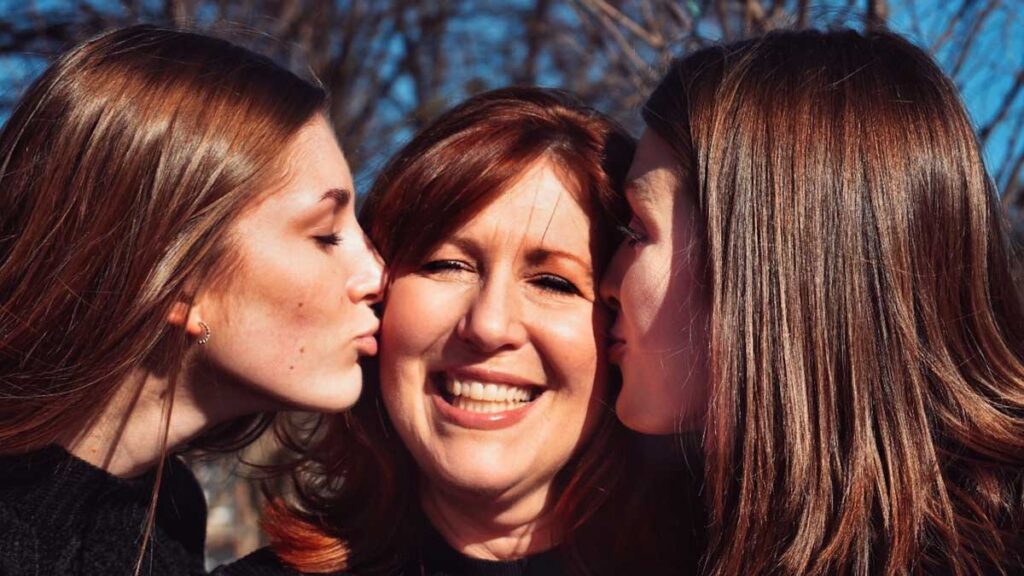 Two grown daughters kiss their mother