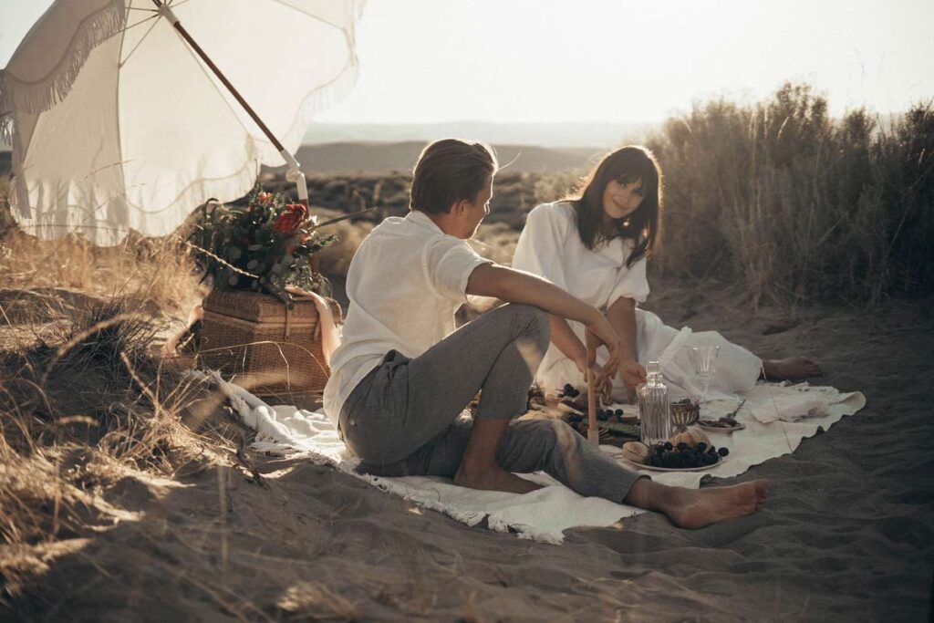 A couple sit on a rug having a picnic