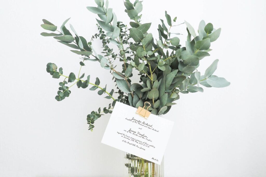 An example wedding invitation postcard attached to a bunch of eucalyptus branches
