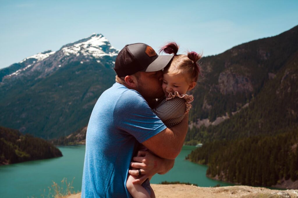 A dad kisses his toddler in front of a mountainous backdrop
