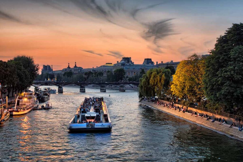The River Seine makes for a very romantic city view, at sunset with a boat cruising on it.