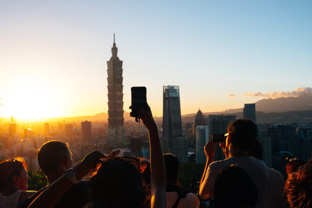 People taking photos on phones of the Taipei skyline in the sunset