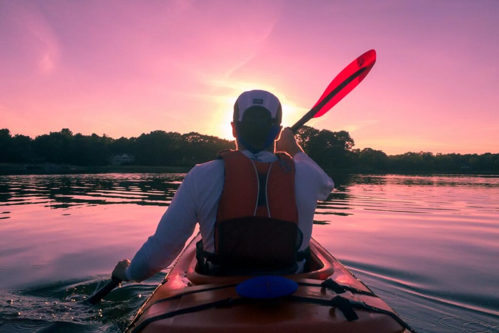 A man seen from behind kayaking on a lake at sunset