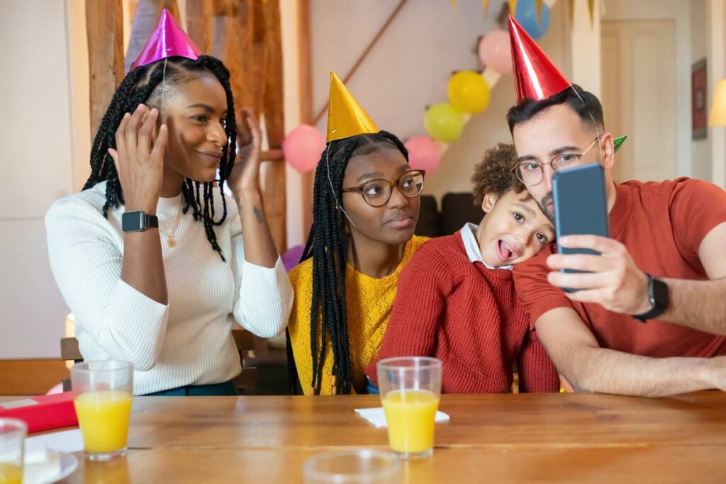 A family looking into their phone camera with birthday party hats on