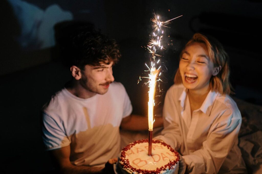 A woman laughs as she holds her birthday cake with a sparkler lit, standing next to her boyfriend.