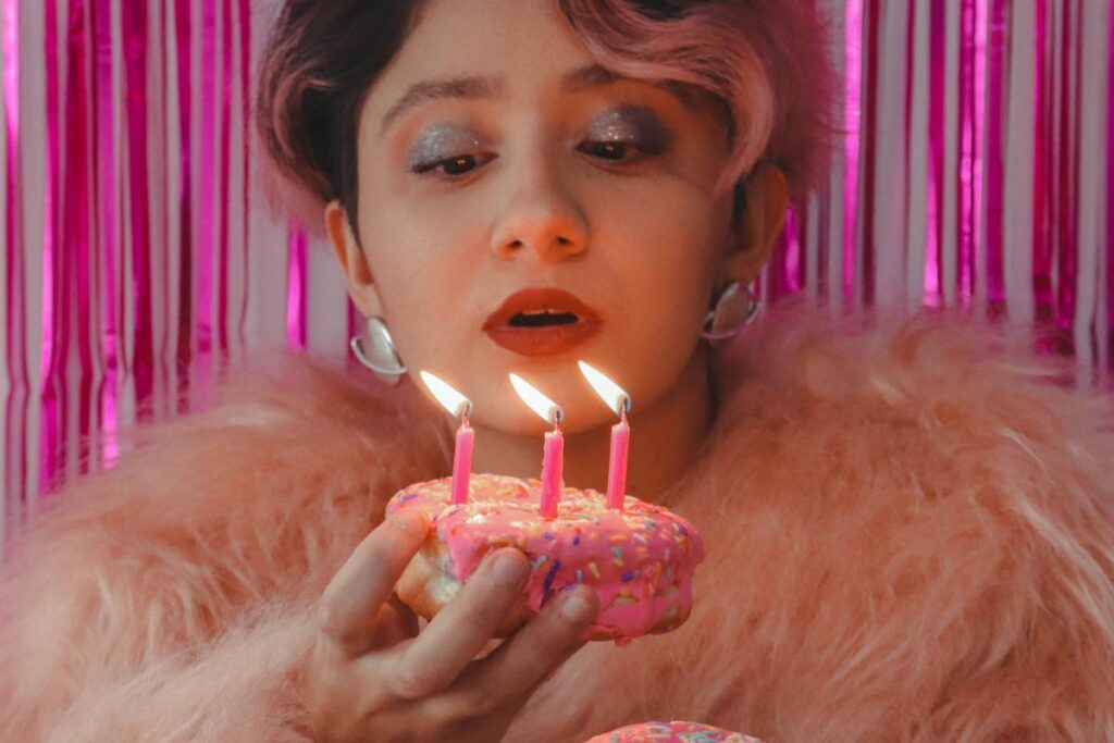 A woman dressed for a party blows out 3 candles on a donut