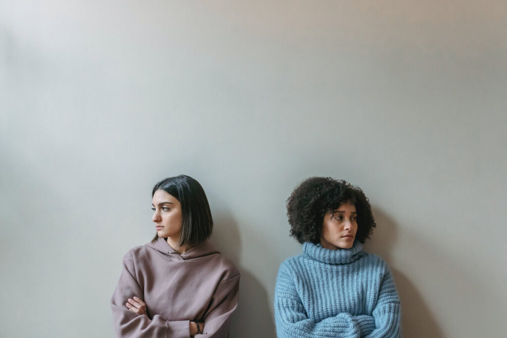 Two women sit looking away from each against a blank wall