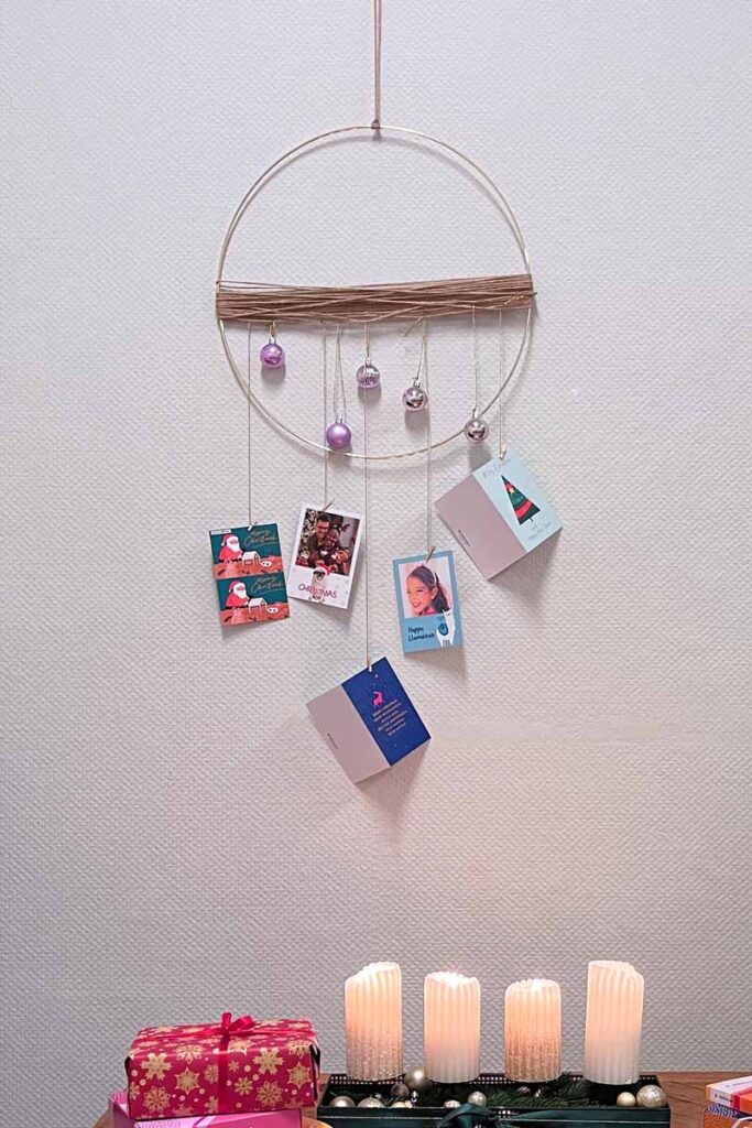 A mobile hanging from a hoop on the wall with Christmas cards hanging on it.