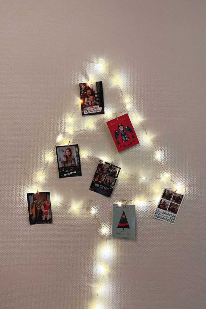 Fairy lights arranged in a Christmas tree shape on the wall, with Christmas cards hanging on it.