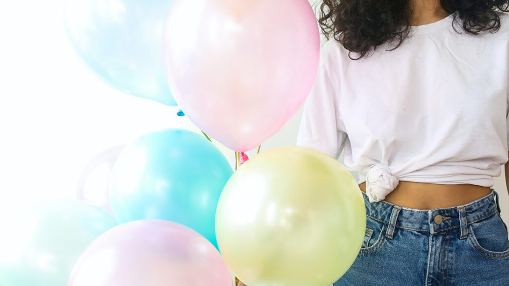 A woman from neck down, holds pastel colored balloons