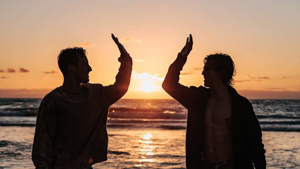 Two brothers high five in front of the sunset on the beach