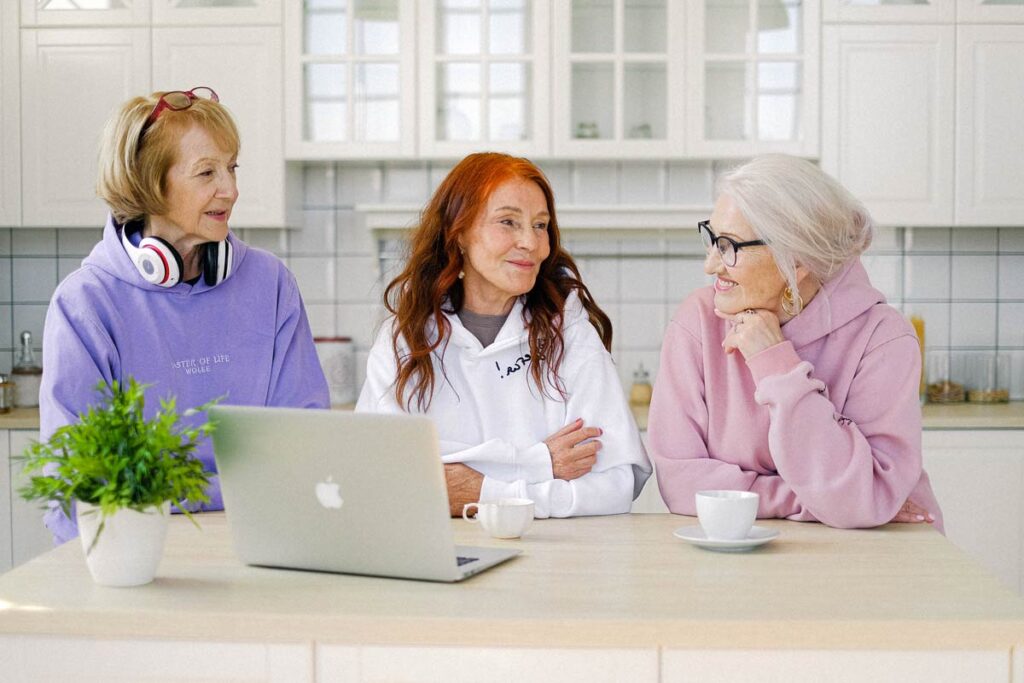 Eine Gruppe von frei altere Frauen sitzen vor einem Laptop and versuchen über Social Media mit alten Freunden wieder Kontakt aufzunehmen