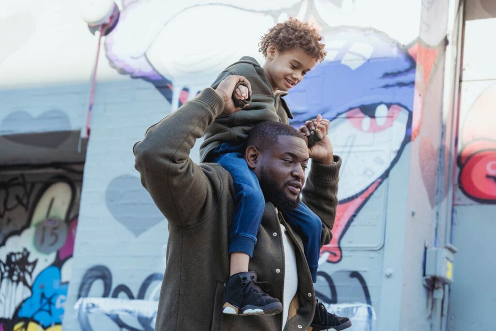 father's day ideas for city tour - a man carries his child on his shoulders with a city backdrop.