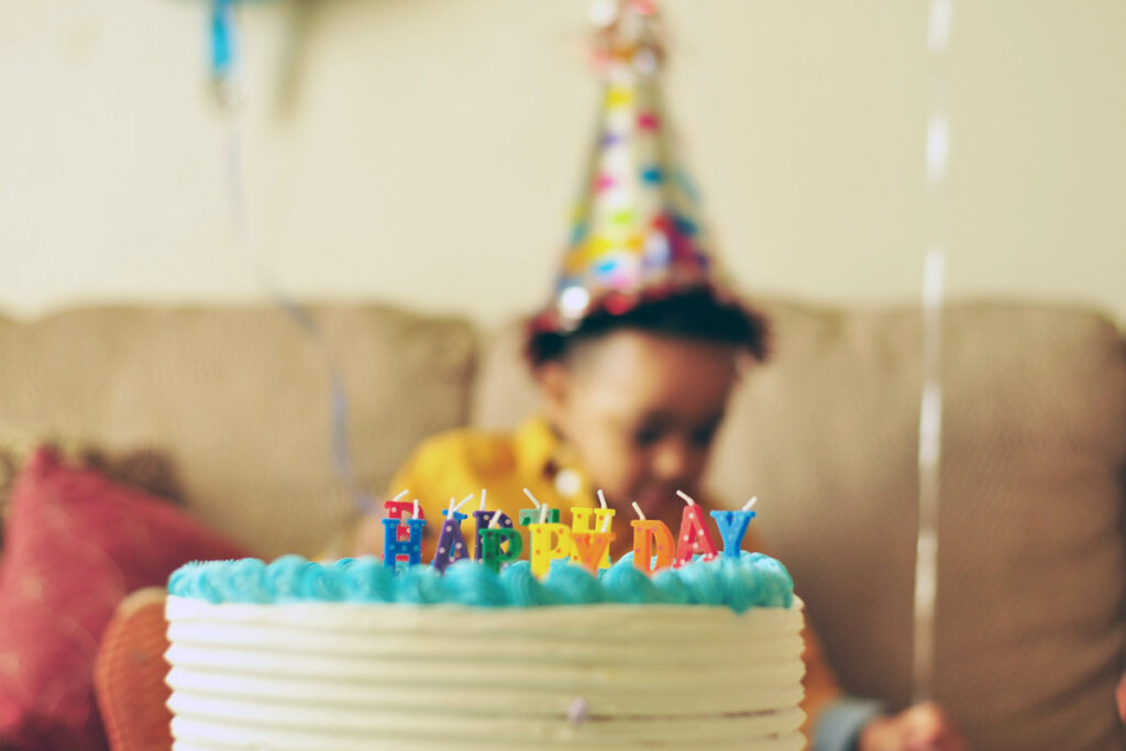 A cake in front of a toddler with a birthday hat on